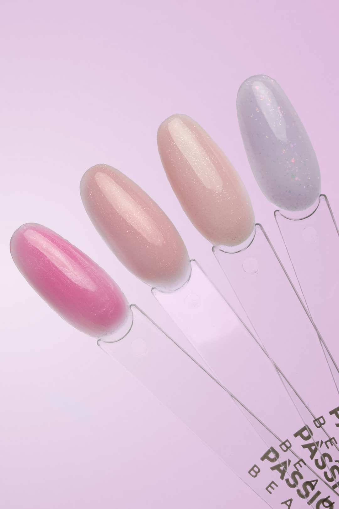 Tip Passione Beauty con smalti gel rosa bubblegum, nude rosato, beige shimmer e lilla glitterato su sfondo viola.