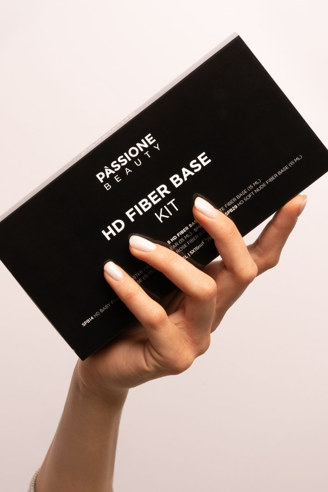 Mano che regge la scatola HD Fiber Base Kit di Passione Beauty, con unghie corte smalto bianco latte lucido effetto naturale.